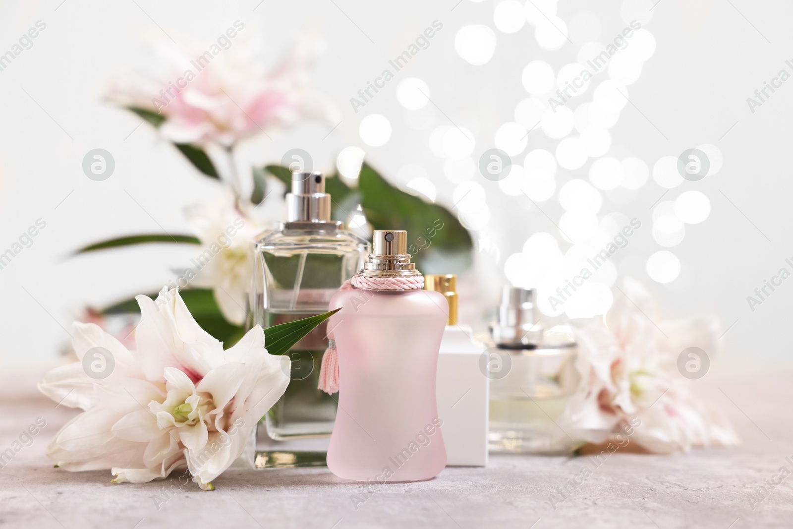 Photo of Perfume bottles and bouquet of beautiful lily flowers on table against beige background with blurred lights, closeup