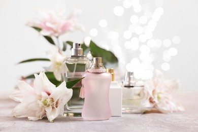 Perfume bottles and bouquet of beautiful lily flowers on table against beige background with blurred lights, closeup