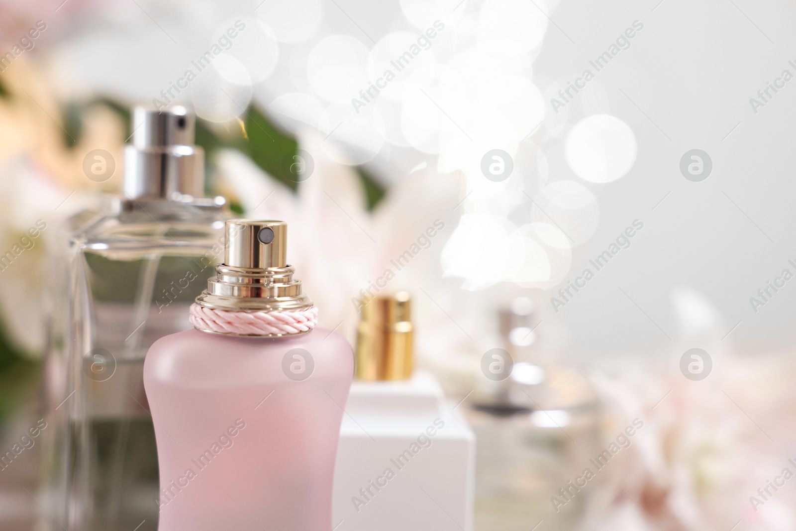 Photo of Bottles of perfume against beautiful lily flowers and blurred lights, closeup. Space for text