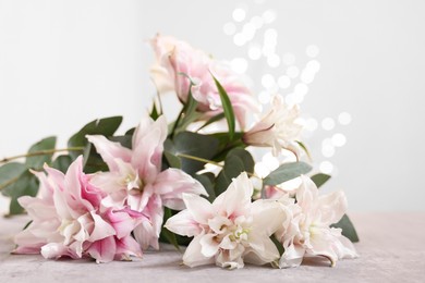 Photo of Bouquet of beautiful lily flowers on table against beige background with blurred lights, closeup