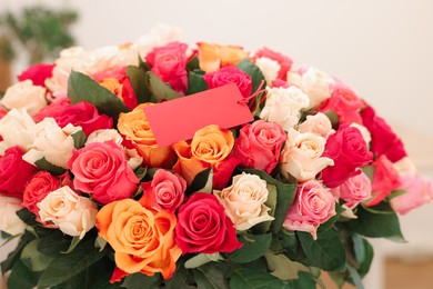 Bouquet of beautiful roses with blank card on blurred background, closeup