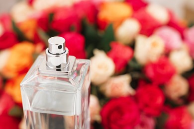 Photo of Bottle of perfume against bouquet of beautiful roses, closeup. Space for text
