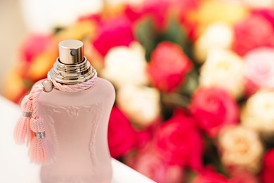 Photo of Bottle of perfume on white table against bouquet of beautiful roses, closeup. Space for text