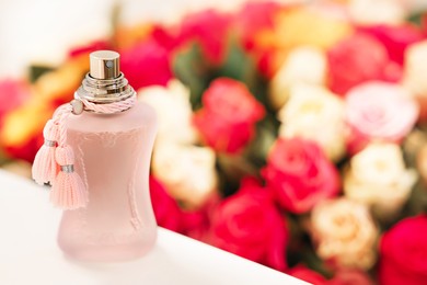 Photo of Bottle of perfume on white table against bouquet of beautiful roses. Space for text