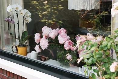 Photo of Beautiful pink peonies in vase and other flowers on window sill, view from outside