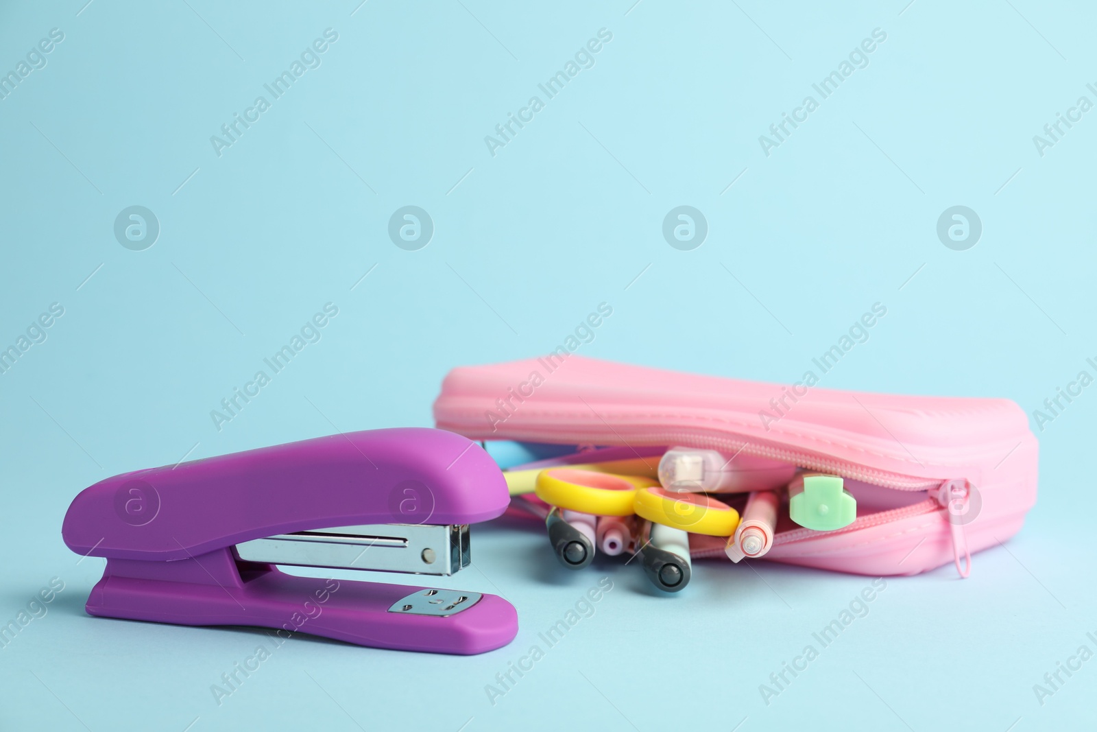 Photo of Violet stapler and other stationery on light blue background, closeup