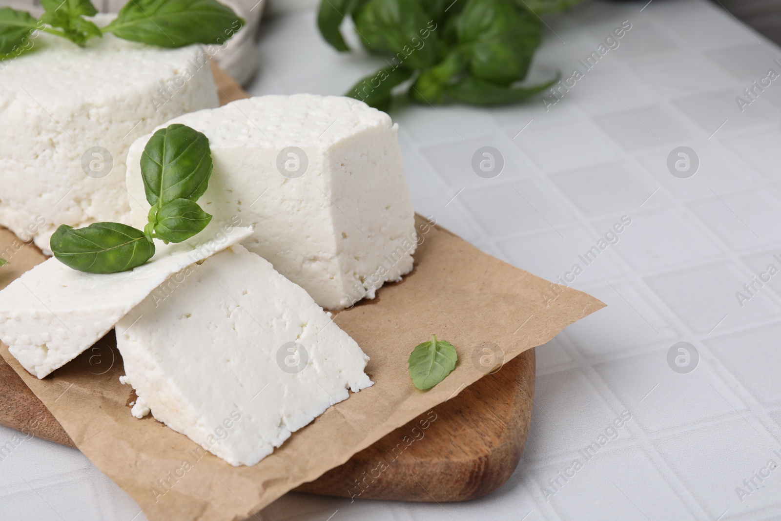 Photo of Fresh ricotta (cream cheese) and basil on white tiled table, closeup. Space for text