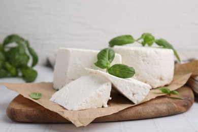 Fresh ricotta (cream cheese) and basil on white tiled table, closeup