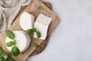 Photo of Fresh ricotta (cream cheese) and basil on white tiled table, top view. Space for text