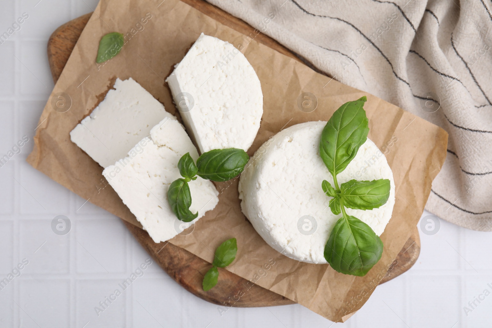 Photo of Fresh ricotta (cream cheese) and basil on white tiled table, top view