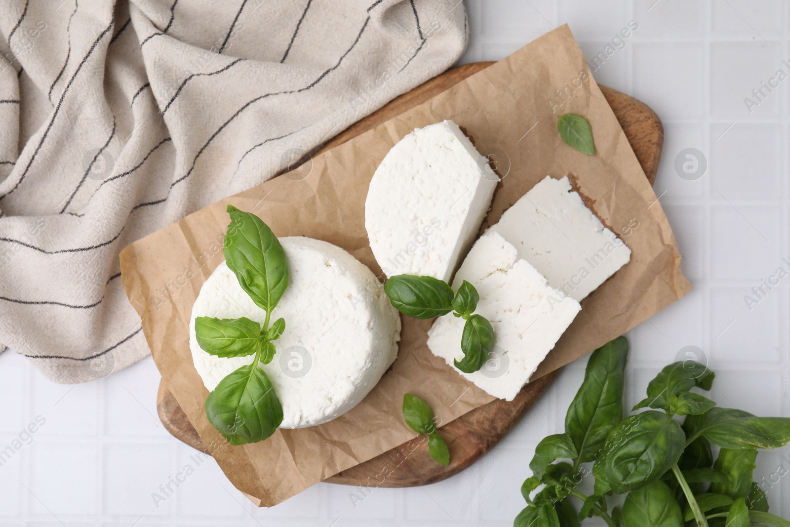 Photo of Fresh ricotta (cream cheese) and basil on white tiled table, top view