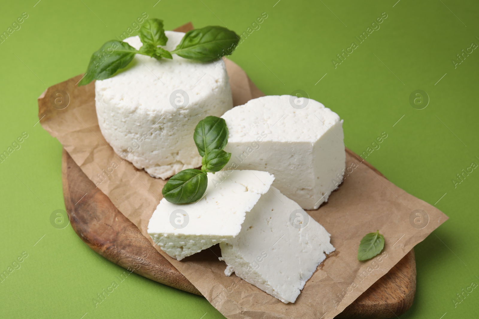 Photo of Fresh ricotta (cream cheese) and basil on green table, closeup