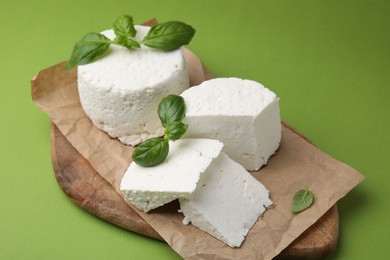 Photo of Fresh ricotta (cream cheese) and basil on green table, closeup