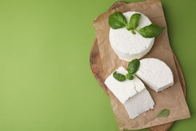 Photo of Fresh ricotta (cream cheese) and basil on green table, top view. Space for text