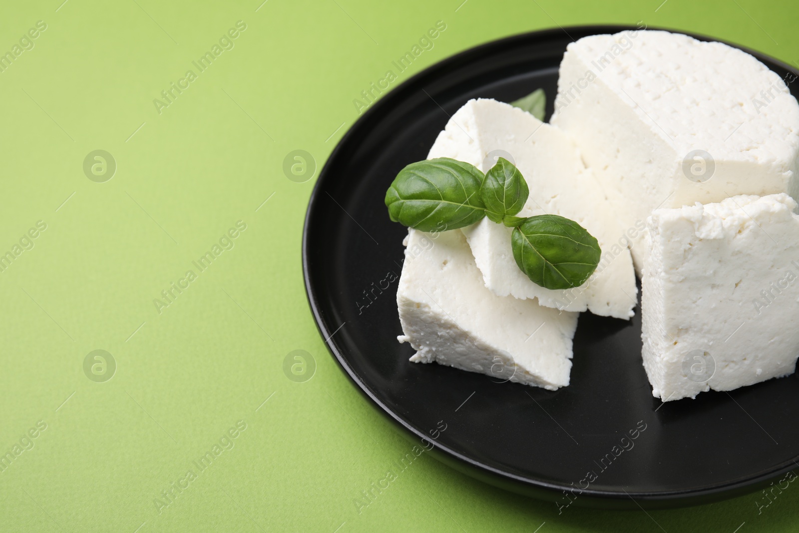 Photo of Fresh ricotta (cream cheese) and basil on green table, closeup. Space for text