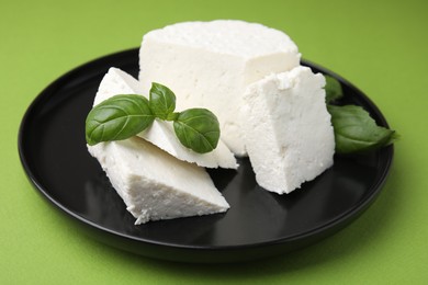 Photo of Fresh ricotta (cream cheese) and basil on green table, closeup