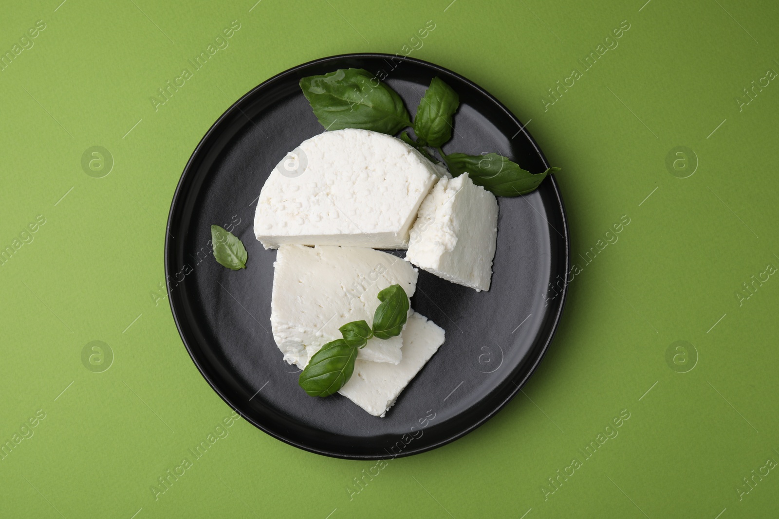 Photo of Fresh ricotta (cream cheese) and basil on green table, top view