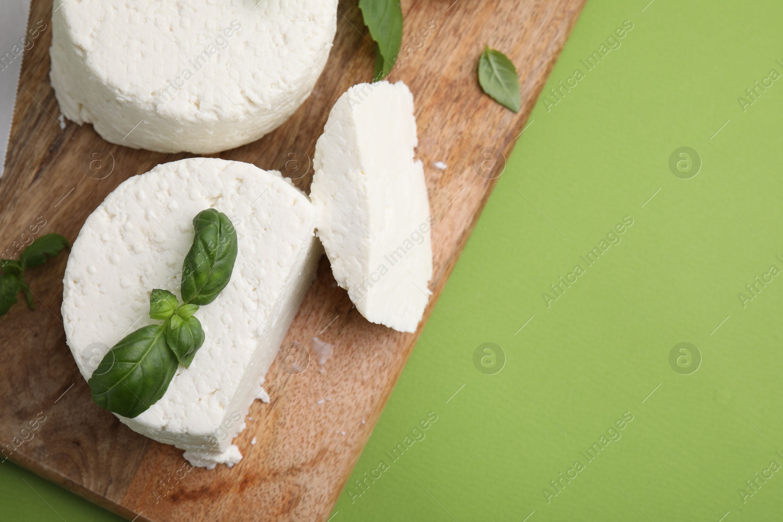 Photo of Fresh ricotta (cream cheese) and basil on green table, top view. Space for text