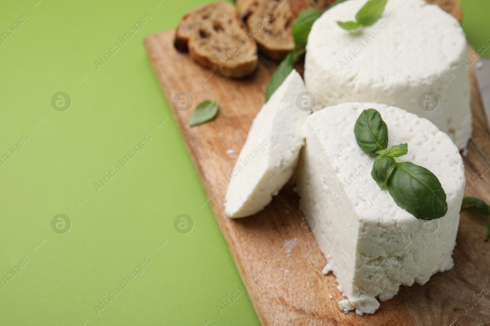 Photo of Fresh ricotta (cream cheese), basil, bread and knife on green table, closeup. Space for text