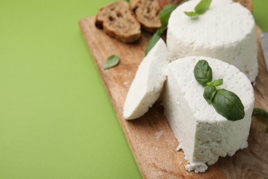 Photo of Fresh ricotta (cream cheese), basil, bread and knife on green table, closeup. Space for text