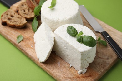 Fresh ricotta (cream cheese), basil, bread and knife on green table, closeup