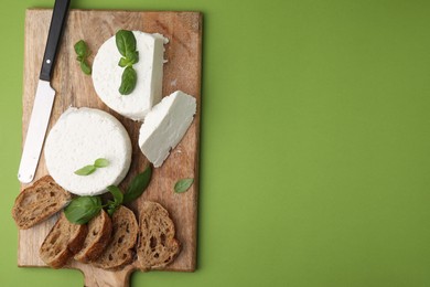 Photo of Fresh ricotta (cream cheese), basil, bread and knife on green table, top view. Space for text