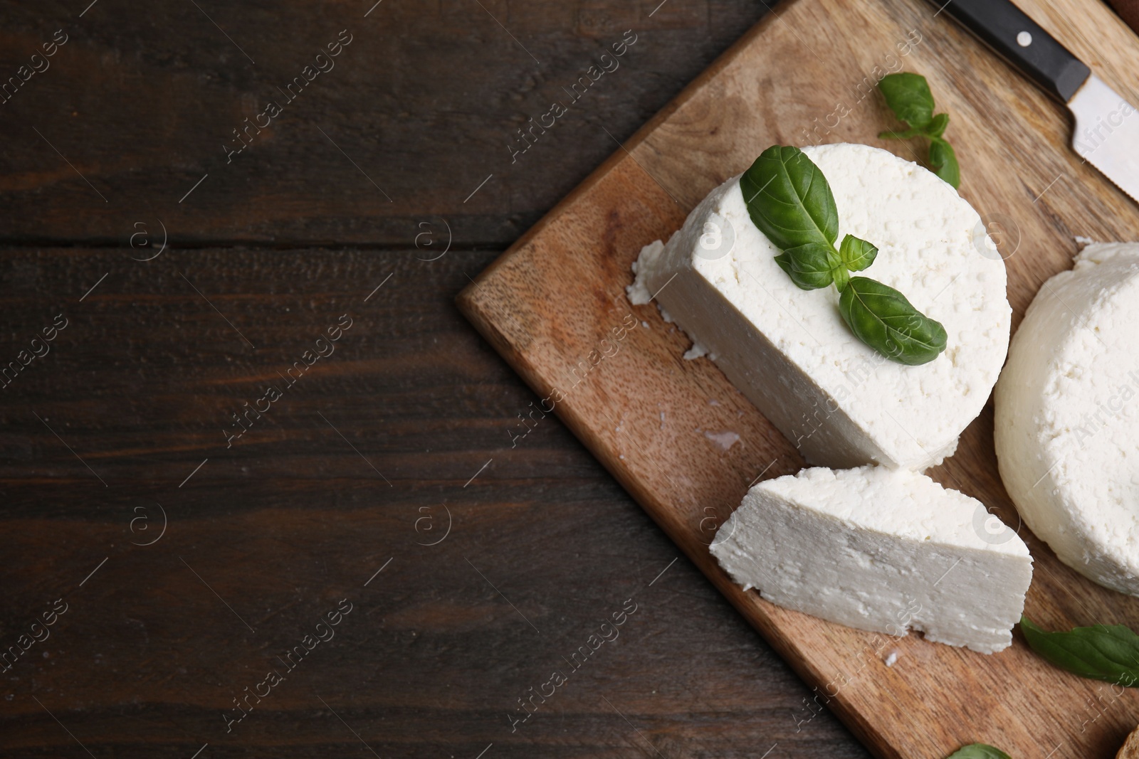 Photo of Fresh ricotta (cream cheese), basil, bread and knife on wooden table, top view. Space for text