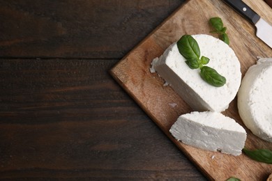 Photo of Fresh ricotta (cream cheese), basil, bread and knife on wooden table, top view. Space for text