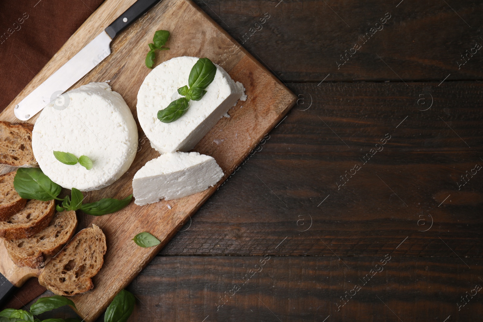 Photo of Fresh ricotta (cream cheese), basil, bread and knife on wooden table, top view. Space for text