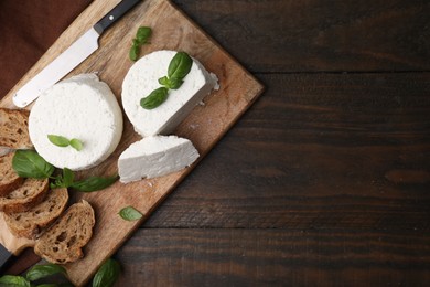 Fresh ricotta (cream cheese), basil, bread and knife on wooden table, top view. Space for text