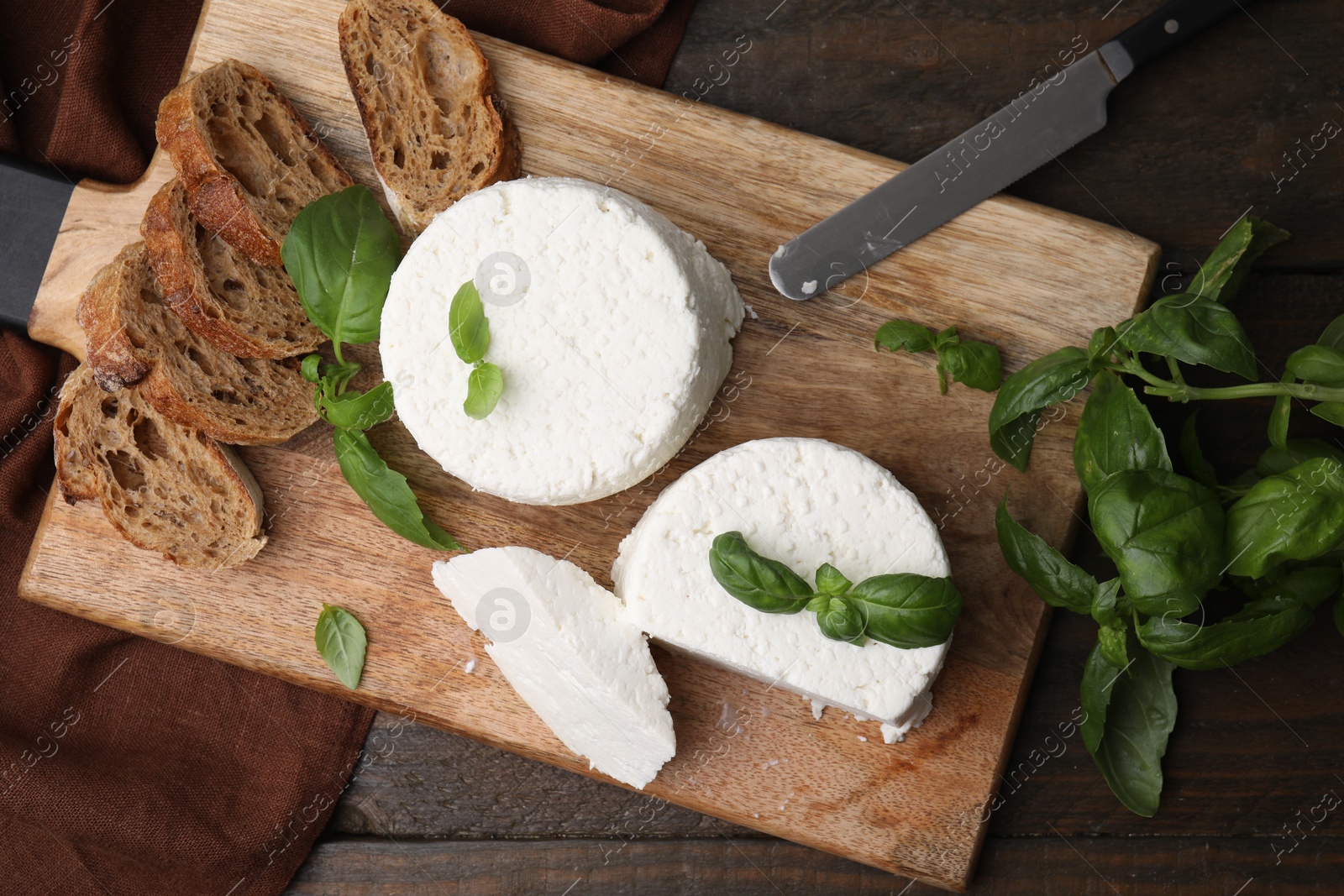 Photo of Fresh ricotta (cream cheese), basil, bread and knife on wooden table, top view