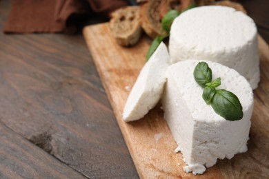 Fresh ricotta (cream cheese) and basil on wooden table, closeup. Space for text