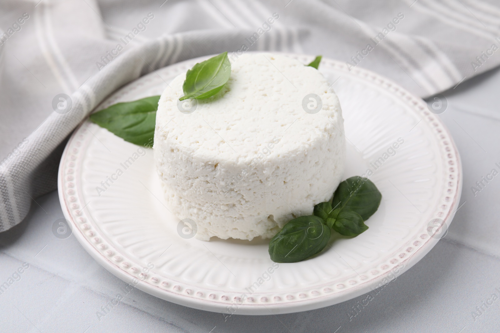 Photo of Fresh ricotta (cream cheese) and basil on light table, closeup