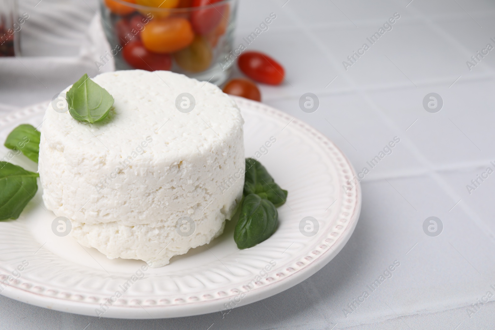 Photo of Fresh ricotta (cream cheese) and basil on light tiled table, closeup. Space for text