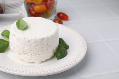 Fresh ricotta (cream cheese) and basil on light tiled table, closeup. Space for text