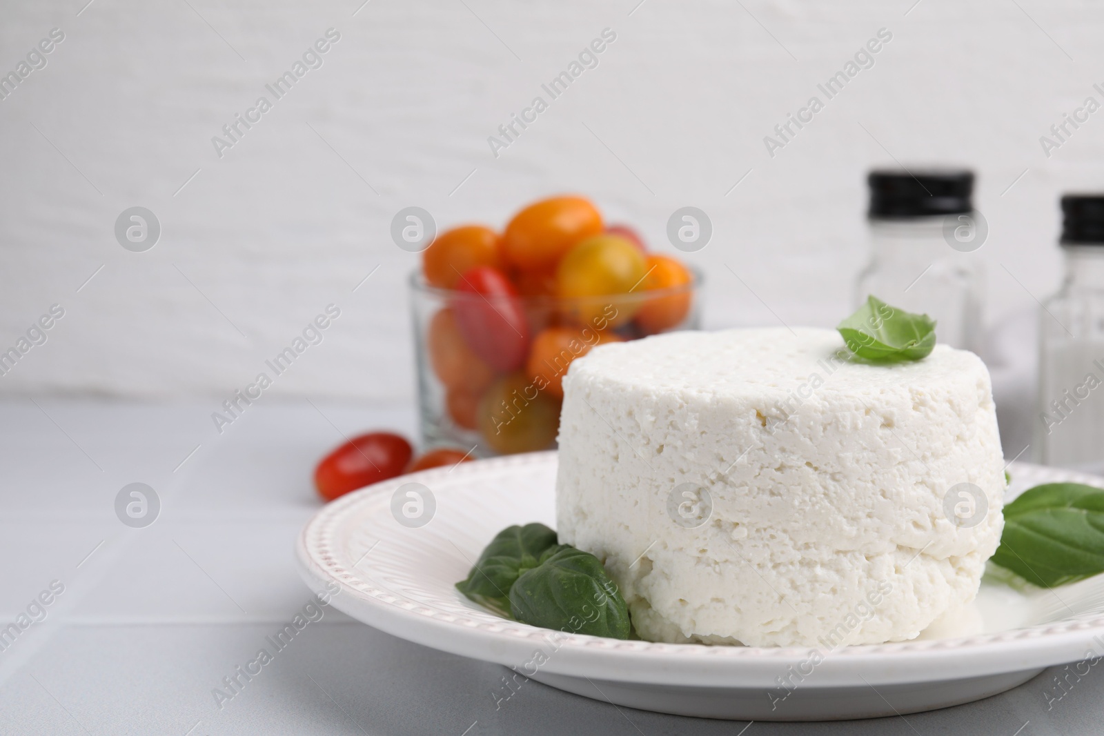 Photo of Fresh ricotta (cream cheese) and basil on light tiled table, closeup. Space for text