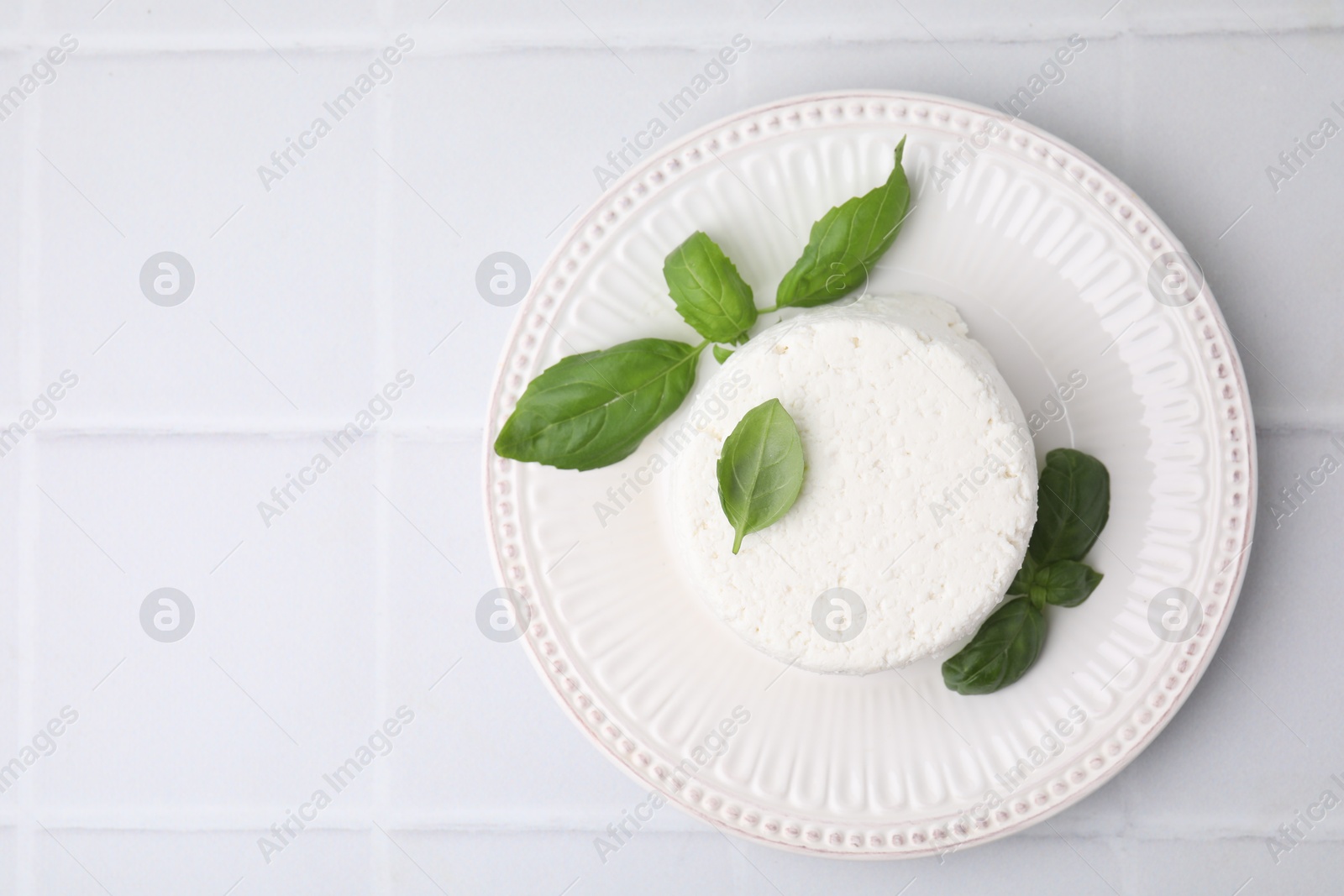 Photo of Fresh ricotta (cream cheese) and basil on light tiled table, top view. Space for text