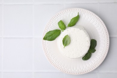 Fresh ricotta (cream cheese) and basil on light tiled table, top view. Space for text