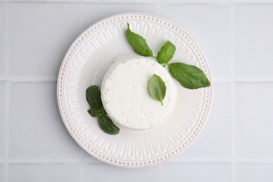 Photo of Fresh ricotta (cream cheese) and basil on light tiled table, top view