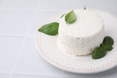 Photo of Fresh ricotta (cream cheese) and basil on light tiled table, closeup. Space for text