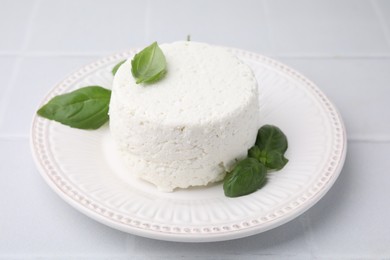 Photo of Fresh ricotta (cream cheese) and basil on light tiled table, closeup