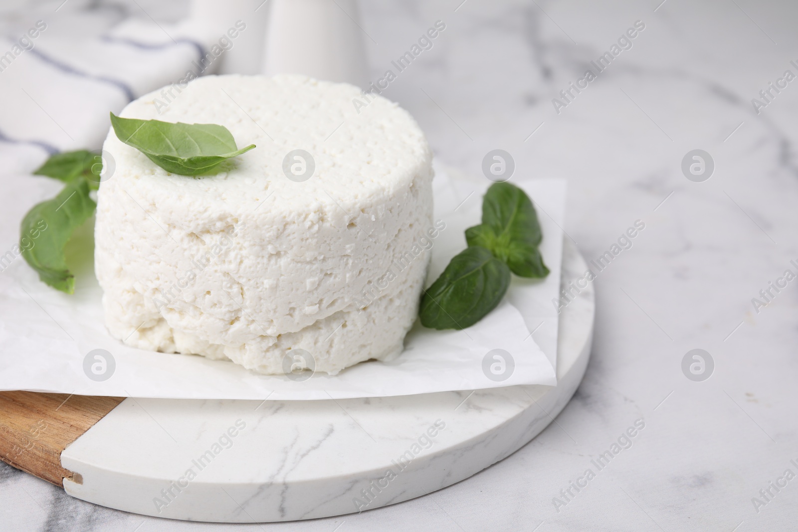 Photo of Fresh ricotta (cream cheese) and basil on light marble table, closeup. Space for text