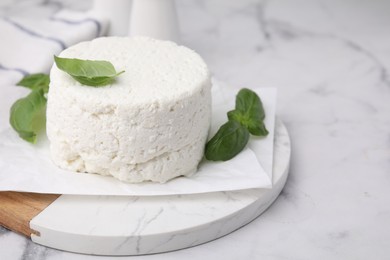 Fresh ricotta (cream cheese) and basil on light marble table, closeup. Space for text