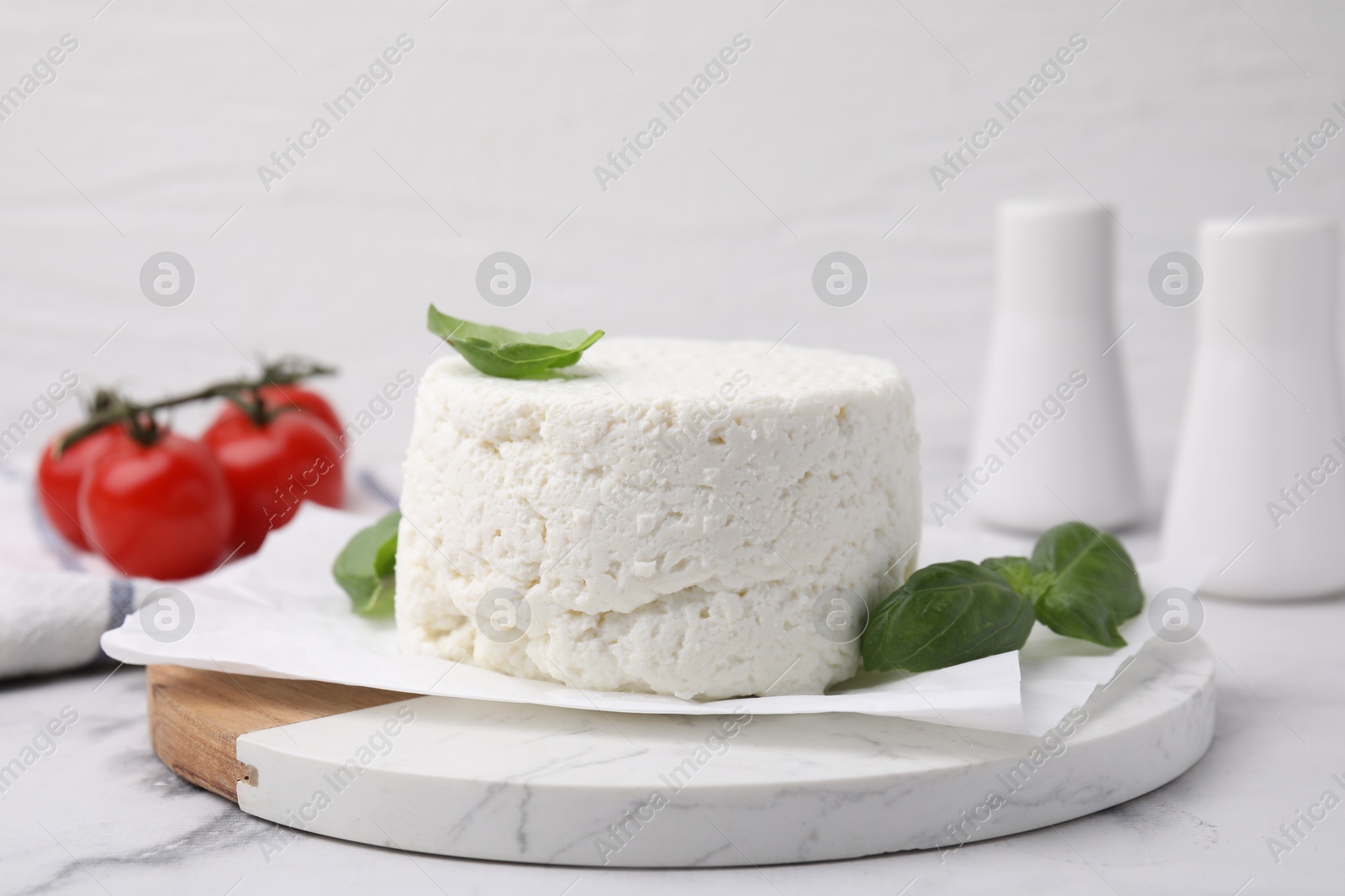 Photo of Fresh ricotta (cream cheese) and basil on light marble table, closeup