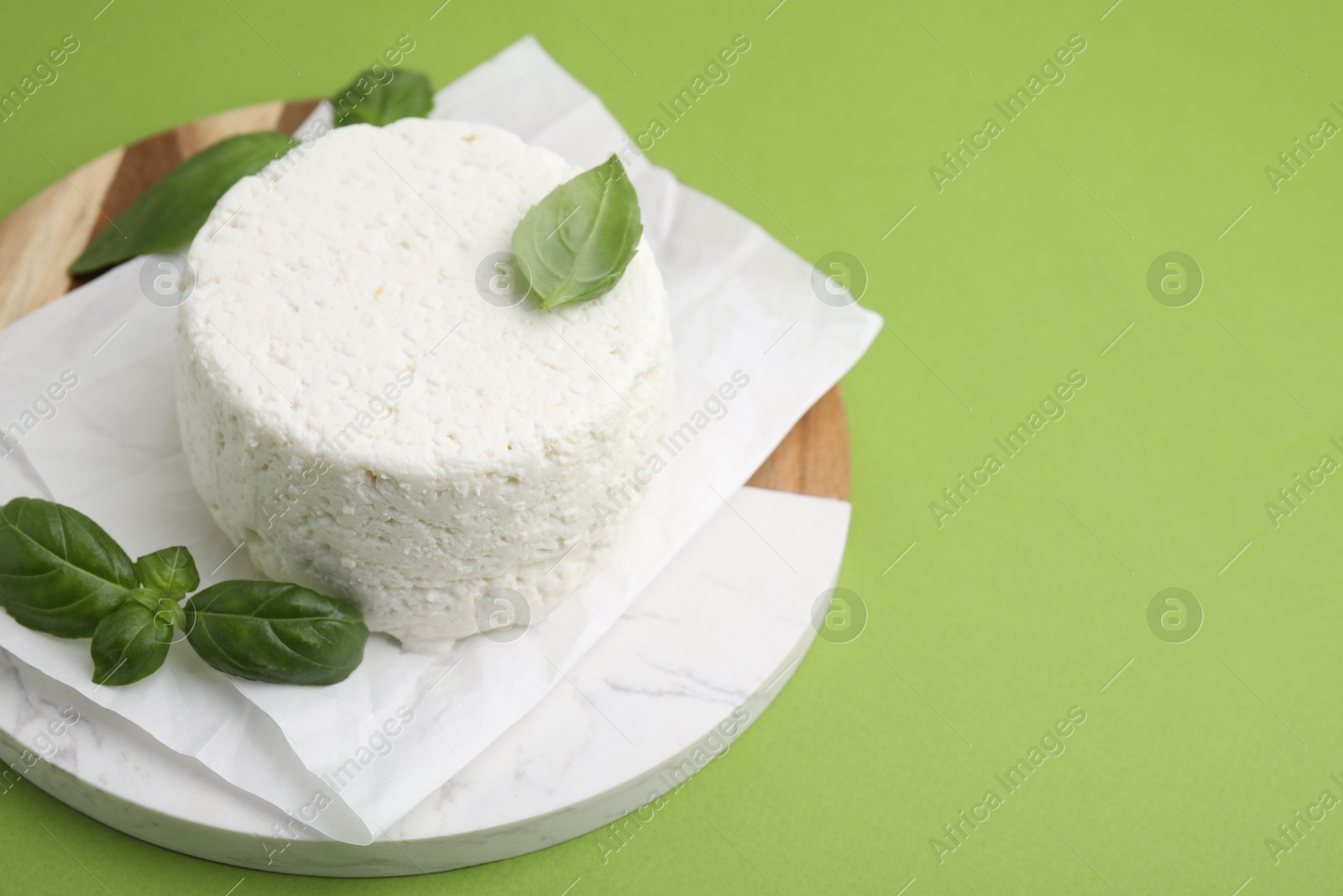 Photo of Fresh ricotta (cream cheese) and basil on green table, closeup. Space for text