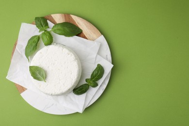 Photo of Fresh ricotta (cream cheese) and basil on green table, top view. Space for text