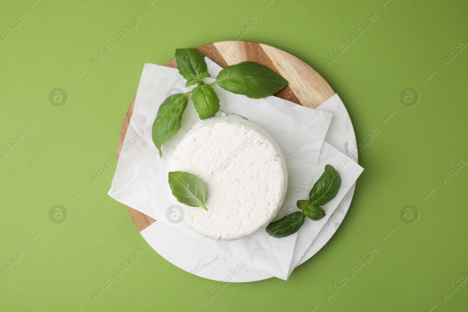 Photo of Fresh ricotta (cream cheese) and basil on green table, top view