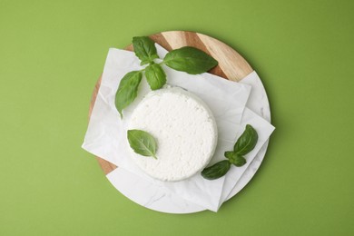 Photo of Fresh ricotta (cream cheese) and basil on green table, top view