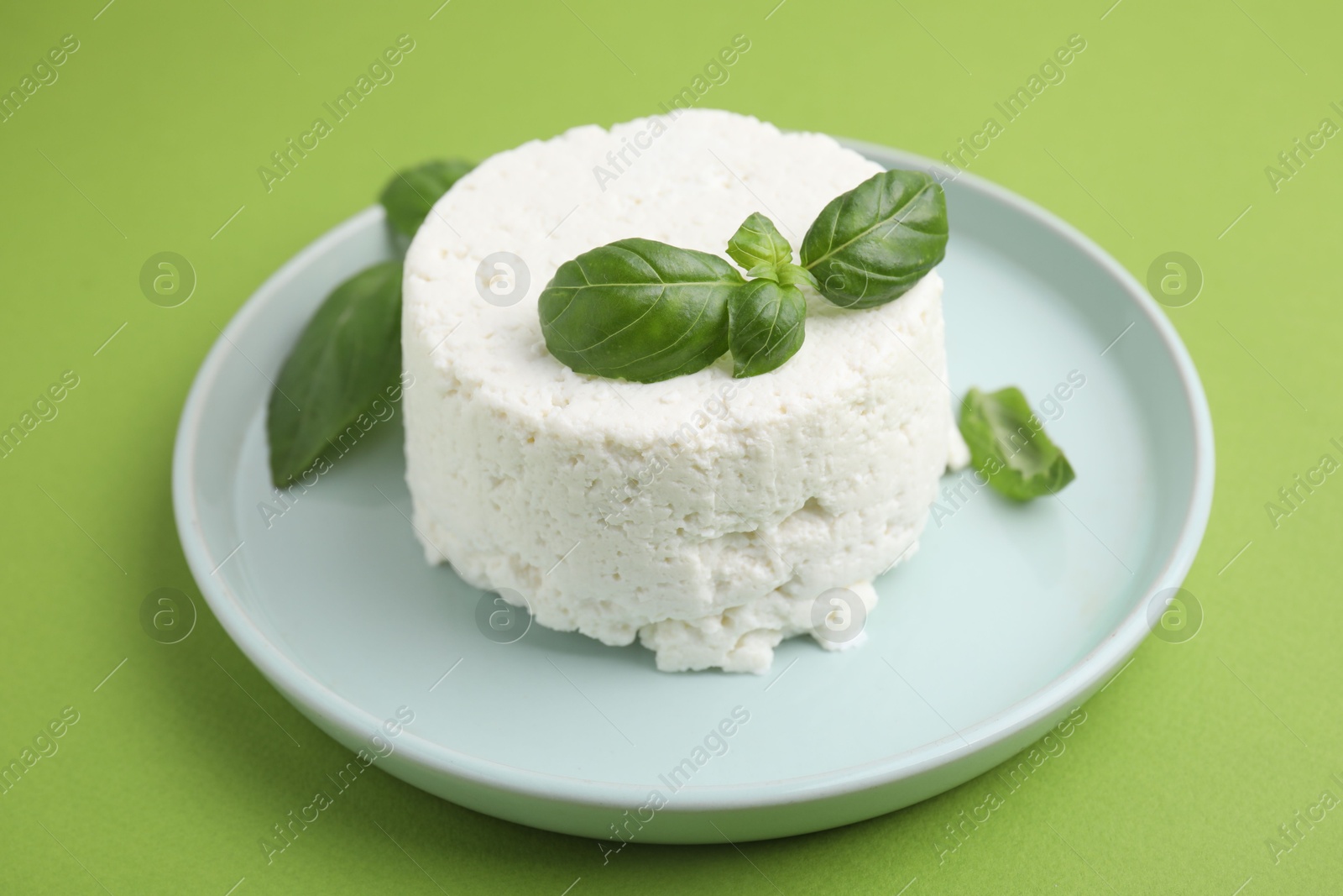 Photo of Fresh ricotta (cream cheese) and basil on green table, closeup