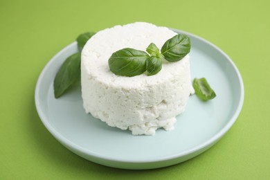 Fresh ricotta (cream cheese) and basil on green table, closeup